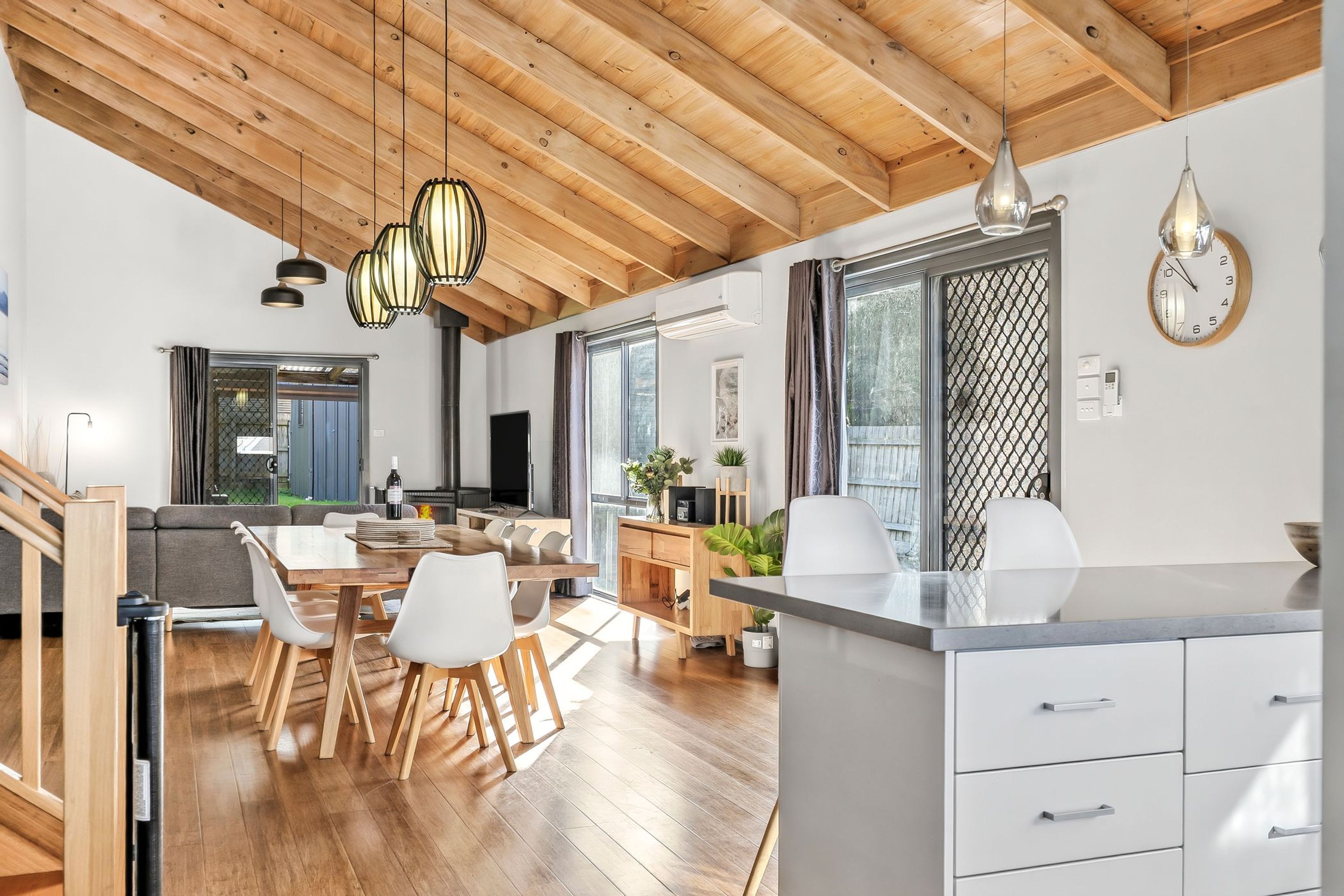 Une cuisine moderne avec un plafond en bois, un coin repas avec une table et des chaises en bois, et une grande fenêtre avec des rideaux.