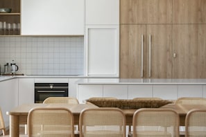 A modern kitchen with white cabinets, a built-in oven, and a dining area with wicker chairs.