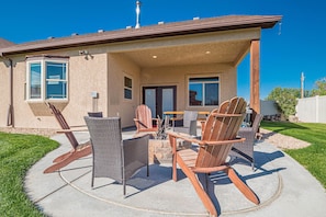 An outdoor patio with wicker chairs and a fire pit, a covered area with a table and chairs, and a house with a chimney and windows. - Black Bear IV: 2 King Suites & Dog-Friendly (Fruita)