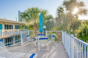 A balcony with white railings, a glass table, and blue chairs. - One block from Pompano Beach - condo w/ shared heated pool & sundeck (Pompano Beach)