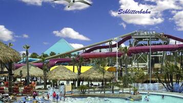 A water park with a large pool, water slides, and thatched umbrellas.