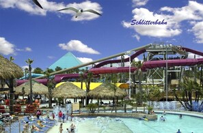Un parc aquatique doté d’une grande piscine, de toboggans et de parasols en chaume.