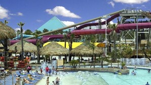 Een waterpark met een groot zwembad, glijbanen en rieten parasols.