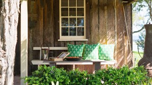 A rustic wooden cabin with a bench, a window, and a small table with a book and a bowl of fruit. - Cox's Cottage in the Hawkesbury Valley (Pitt Town)