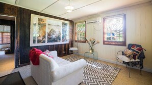 A cozy living room with a white sofa, a patterned rug, a chair with a blanket, and artwork on the wall. - Cox's Cottage in the Hawkesbury Valley (Pitt Town)
