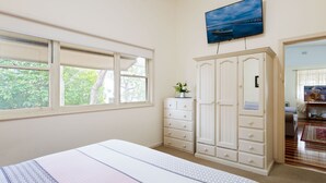 A bedroom with a bed, a dresser, a wardrobe, a television, and a window with a view of trees. - Daves Place, 27 Rigney St - Holiday house with Wifi, Dog Friendly, Aircon & Boat Parking (Shoal Bay)