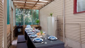 An outdoor dining area with a long table set for a meal, surrounded by wooden walls and a view of greenery. - Daves Place, 27 Rigney St - Holiday house with Wifi, Dog Friendly, Aircon & Boat Parking (Shoal Bay)