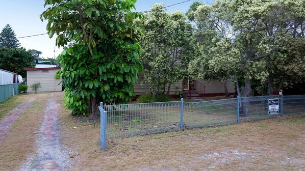 Patio cercado con un árbol grande, un edificio pequeño y un cartel que indica que es una propiedad de alquiler.
