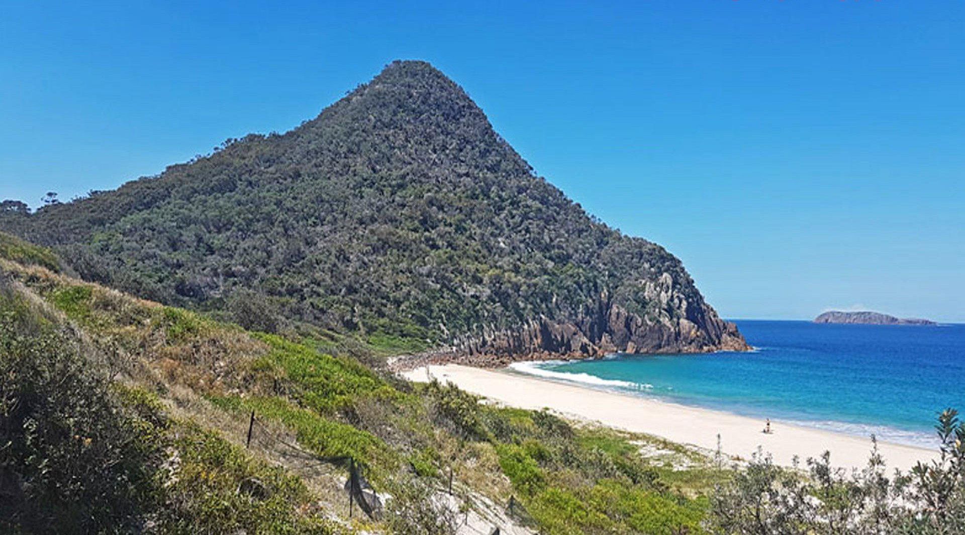 A coastal landscape with a prominent hill, a sandy beach, and the ocean.