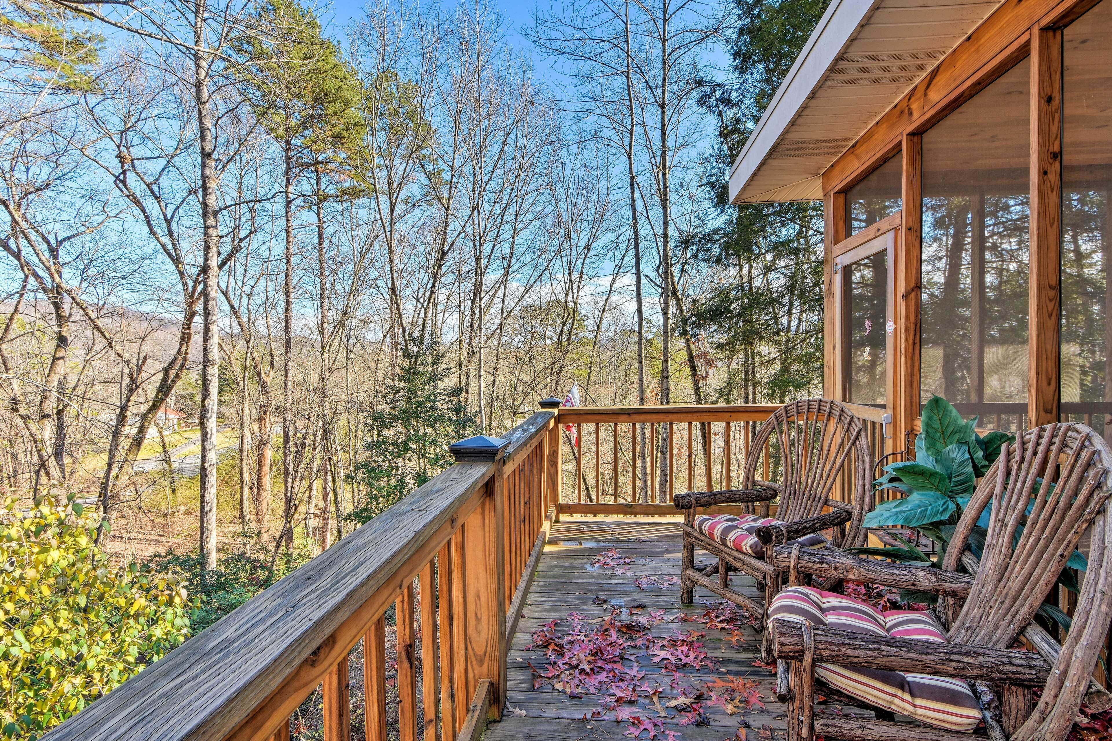A wooden deck with a railing, two wicker chairs with cushions, and a view of a forested area.
