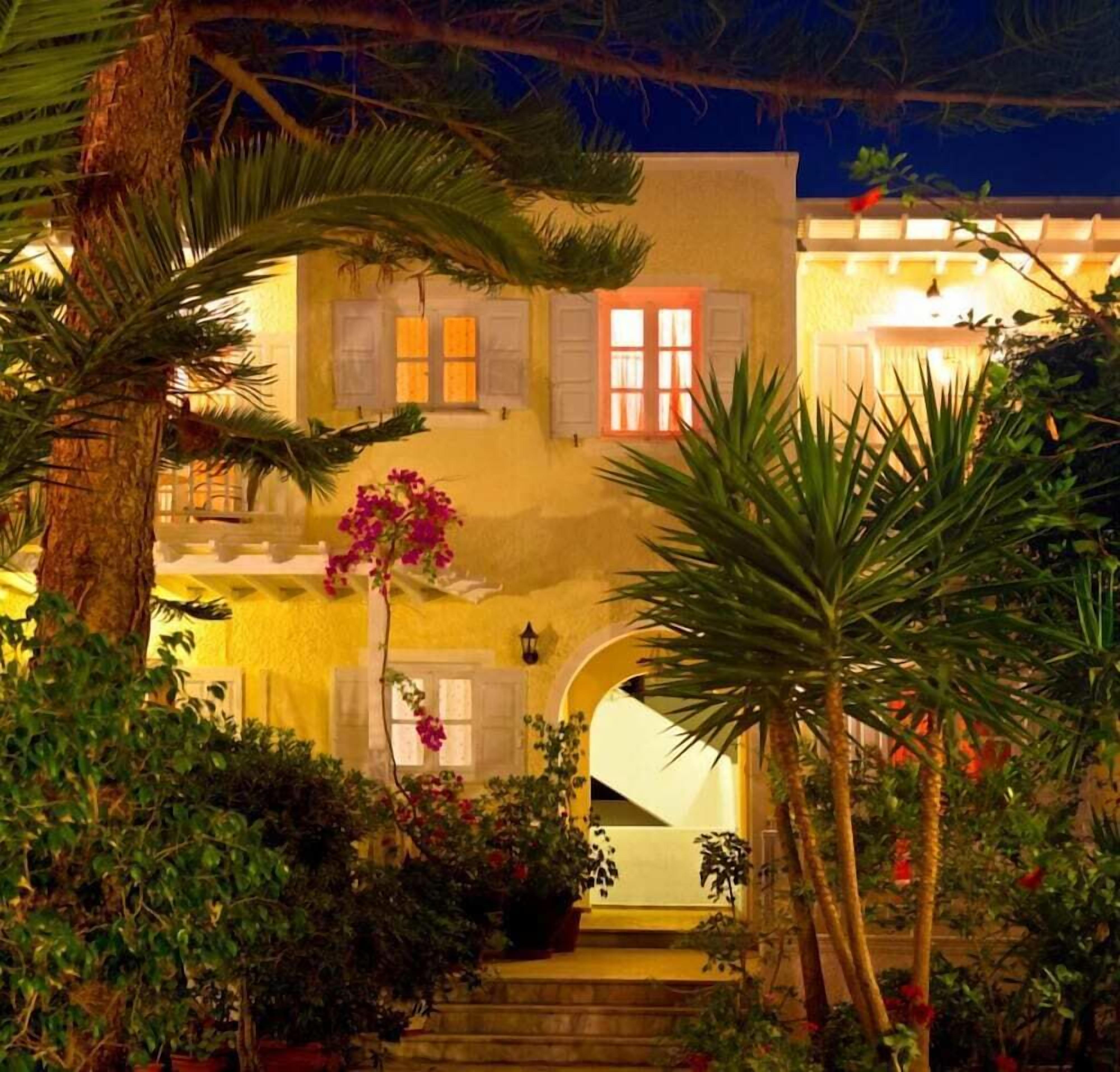 A building with a staircase leading to a door, surrounded by greenery and palm trees.