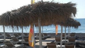 Una playa con sombrillas de paja, sillas reclinables blancas y una terraza de madera.