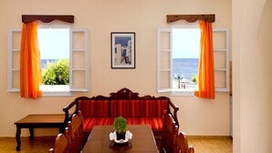 Una habitación con una mesa de madera, sofá tapizado en rojo y dos ventanas con cortinas naranjas.