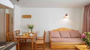 Una habitación acogedora con una mesa de madera para comer, sillas, un sofá y una peque ña mesa con un florero.