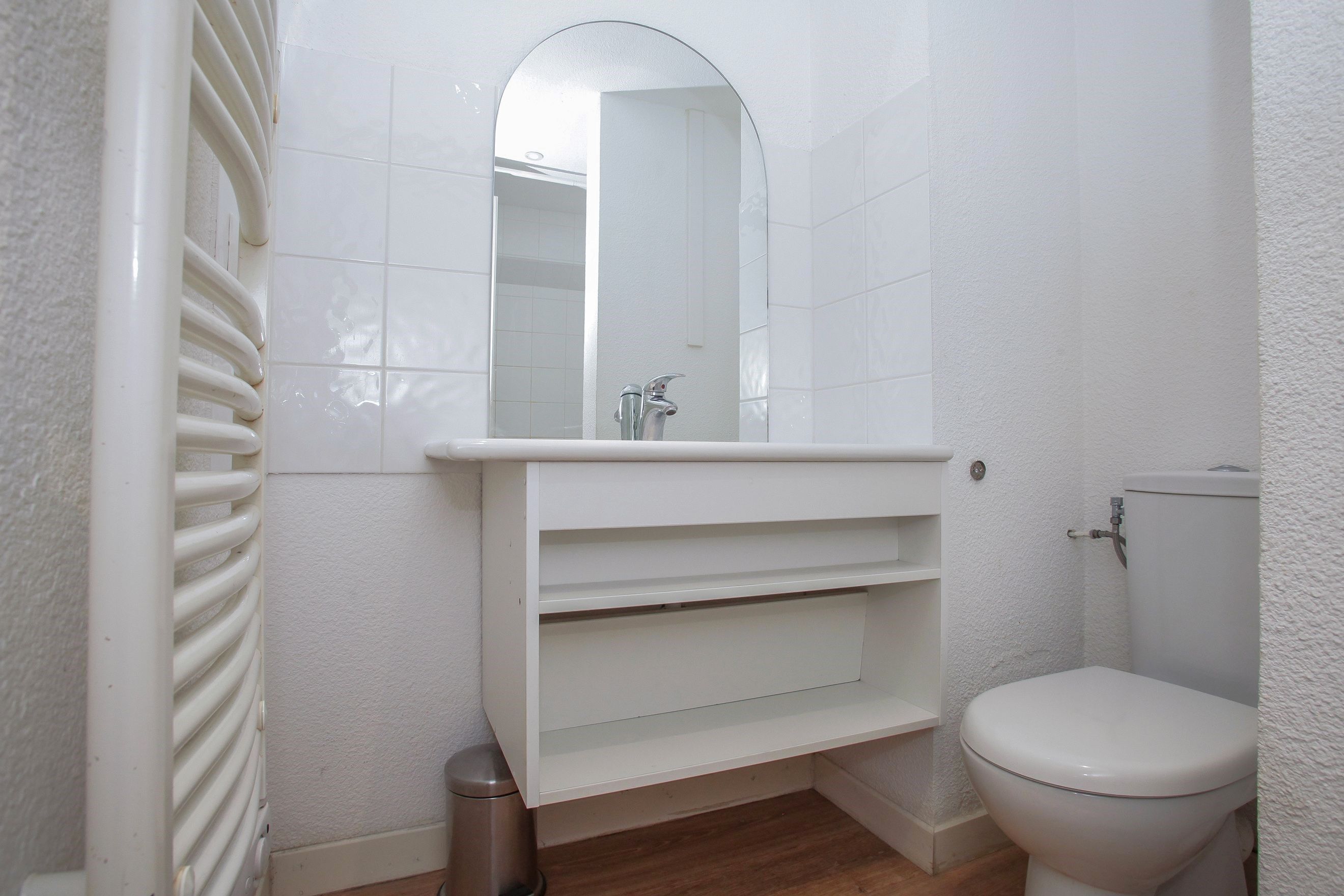 Un baño con un inodoro blanco, un lavabo con un espejo encima y un radiador.