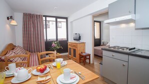 Une pièce chaleureuse avec une table à manger en bois, mise pour le petit-déjeuner, un coin cuisine avec une cuisinière et une fenêtre avec des rideaux.