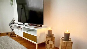 A modern living room with a white entertainment unit, a flat-screen TV, a small side table, and two candles on wooden stands. - SnowKaya Appartement/Fewo 5-Bettwohnung by Interhome (Engelberg)