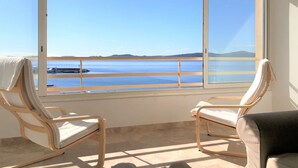 A room with two chairs facing a large window overlooking a body of water and a distant landmass.