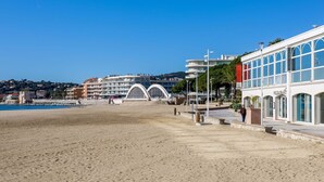 A beachside hotel with a modern architectural design, featuring a prominent arched entrance and a clear view of the sea.