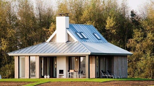 A modern house with a metal roof, large windows, and a patio area with chairs. - Oesterdam Resort by Interhome (Tholen)