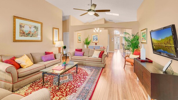 A spacious living room with a sofa set, a coffee table, a TV, and a ceiling fan. - PRIVATE Pool, 3mi to Disney, Forest view with total privacy, Game room (Kissimmee)