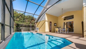 An indoor swimming pool with clear glass walls, a sunlit patio area with outdoor furniture, and a view of trees outside. - PRIVATE Pool, 3mi to Disney, Forest view with total privacy, Game room (Kissimmee)