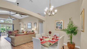 A dining area with a glass table, white chairs, and red napkins. There is a ceiling fan, a chandelier, and a potted plant. - PRIVATE Pool, 3mi to Disney, Forest view with total privacy, Game room (Kissimmee)