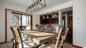 Un comedor con una mesa y sillas de madera, una cocina al fondo y un ventanal grande.