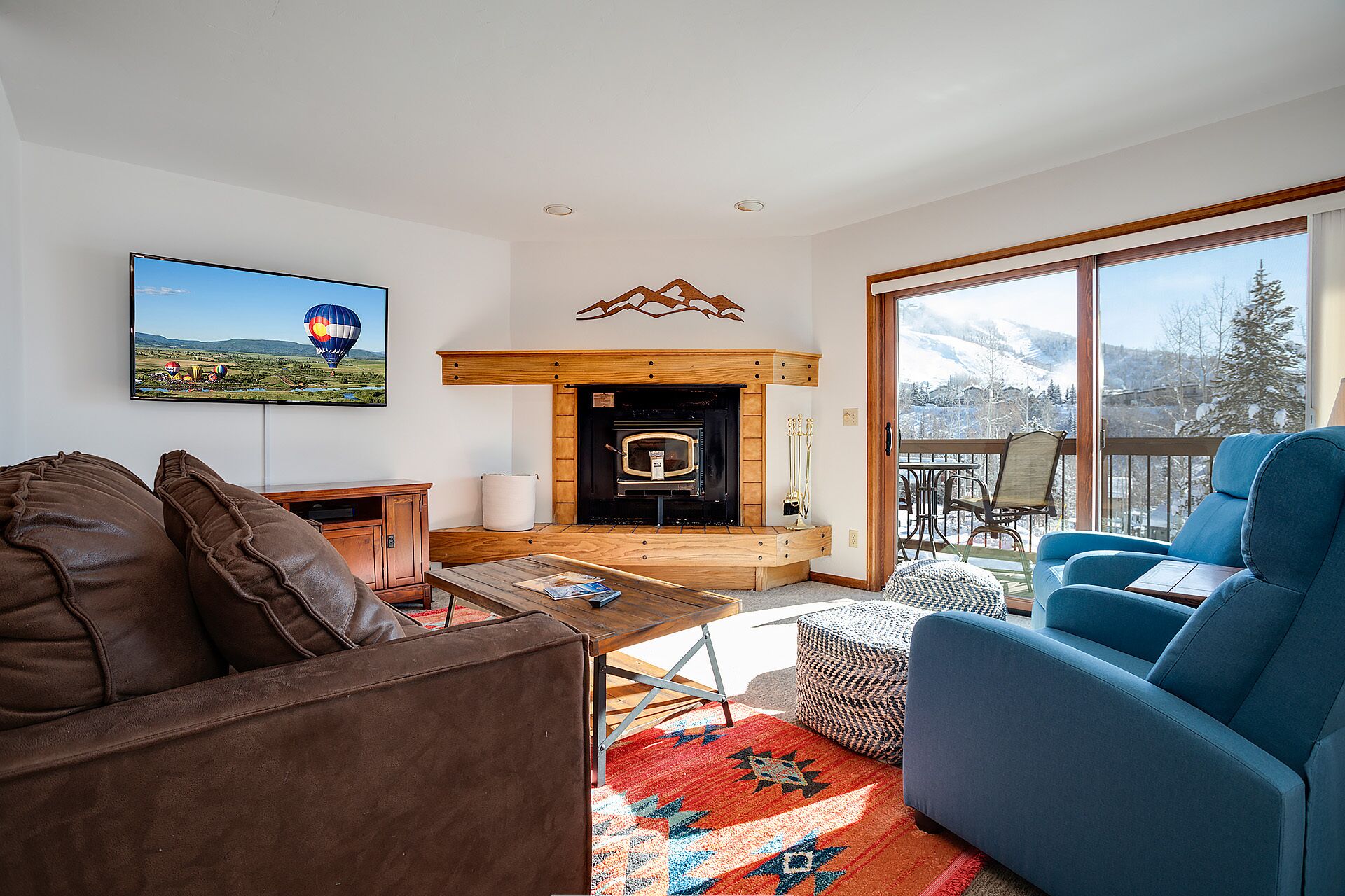 A living room with a fireplace, a television, and a view of a snowy mountain landscape.