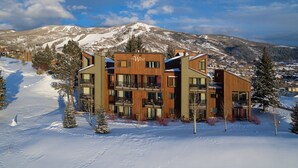 Een modern meerlaags hotel met een skipistes als achtergrond, met balkons en grote ramen.