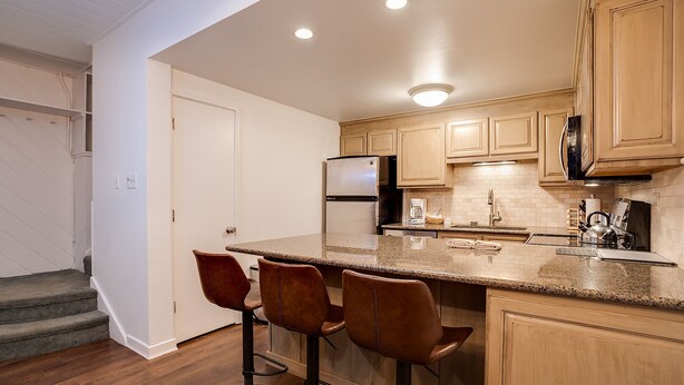 Una cocina con una isla central, taburetes de bar, armarios de madera, un refrigerador y un microondas.