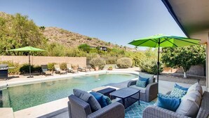 Um quintal com piscina, móveis de jardim e guarda-sóis.