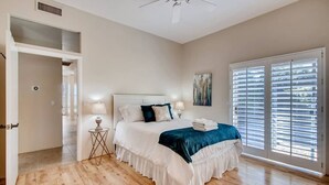 Quarto com cama, abajures, ventilador de teto e janela com persianas.