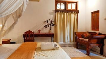 A bedroom with a bed, a desk, a chair, a plant, and a window with curtains.