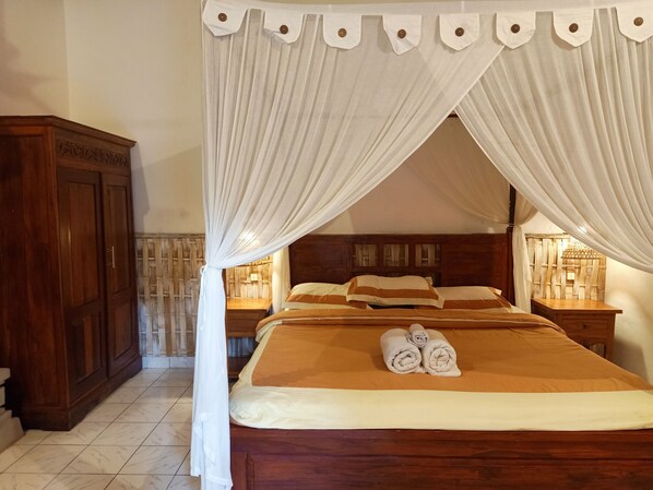 A neatly made bed with a canopy, wooden headboard, and a nightstand with a lamp. - Binaria Museum Hotel (Buleleng)