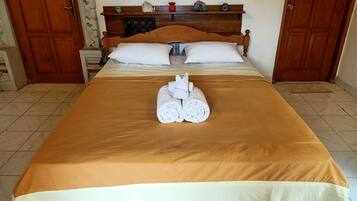 A neatly made bed with a brown bedspread, two white pillows, and two rolled towels placed in front.