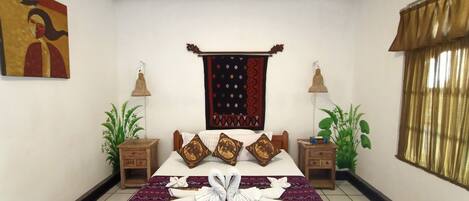 A neatly arranged bedroom with a bed, two nightstands, a wall hanging, and a window with curtains.