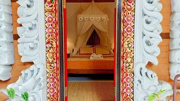 Una habitación con una cama bajo un dosel, suelo de madera y pared roja.