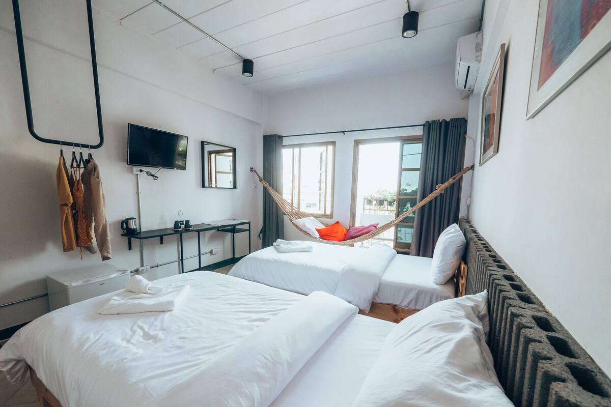 Une chambre d’hôtel avec deux lits, un bureau, une télévision et un hamac.