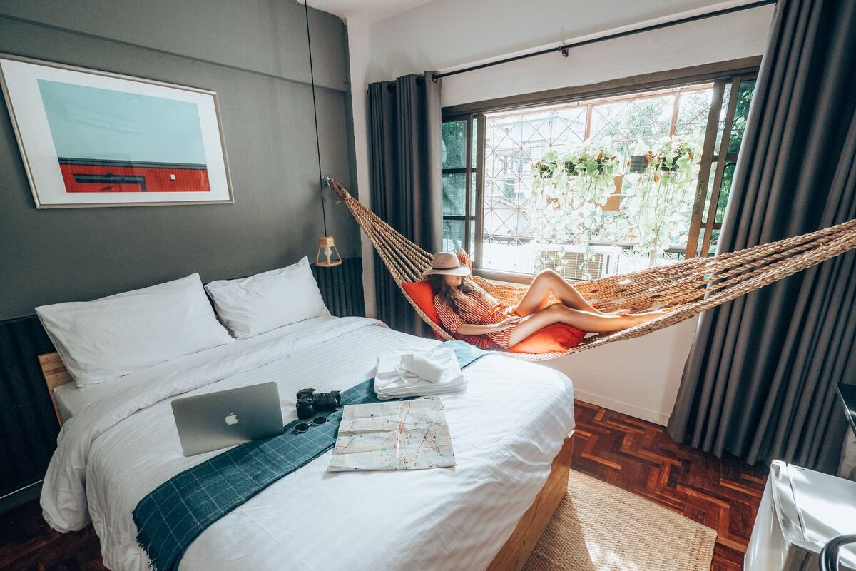 Une chambre à coucher avec un lit, un ordinateur portable, un appareil photo et une carte géographique posée sur le lit.