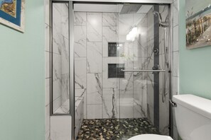 Un baño con cabina de ducha de vidrio, baldosas de mármol, un inodoro blanco y una ventana pequeña.