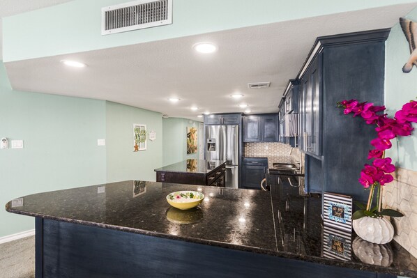 A modern kitchen with dark cabinetry, a granite countertop, and a central island with a bowl.