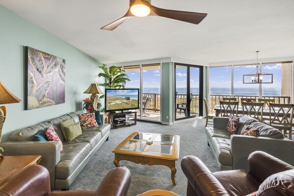 A spacious living room with a large television, leather sofas, a coffee table, and a view of the ocean through large sliding glass doors. - Sea Gull #210: Beachfront 3 bed 2.5 Bathroom With Spectacular Views and 24 Hour Management (Port Aransas)