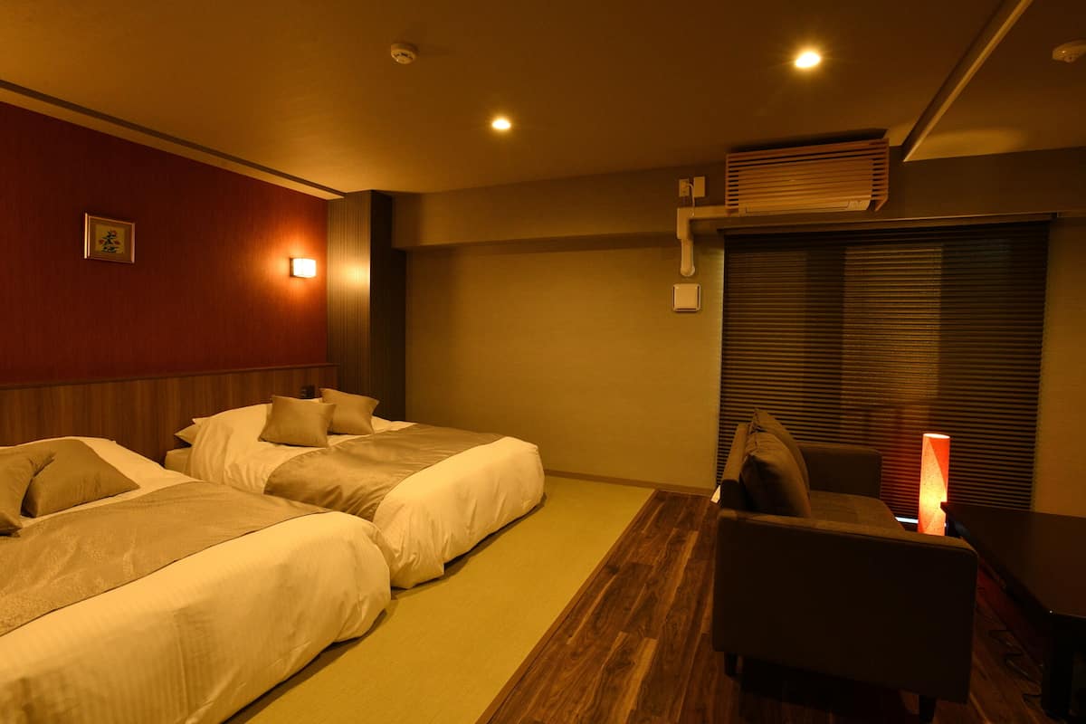 A hotel room with two beds, a desk, a chair, a lamp, and a picture on the wall.