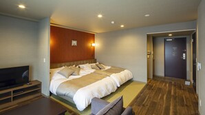 A hotel room with a large bed, a TV, a wooden floor, and a door to the hallway.