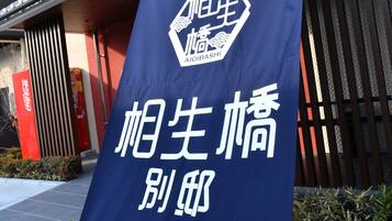 A banner with a logo and Japanese text, hanging outside a building with a sloped roof and metal railings.