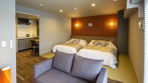 A hotel room with two beds, a sofa, a small kitchen area, and a bathroom.