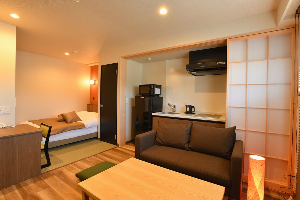 A compact hotel room with a kitchenette, a sofa, a small table, and a bed.