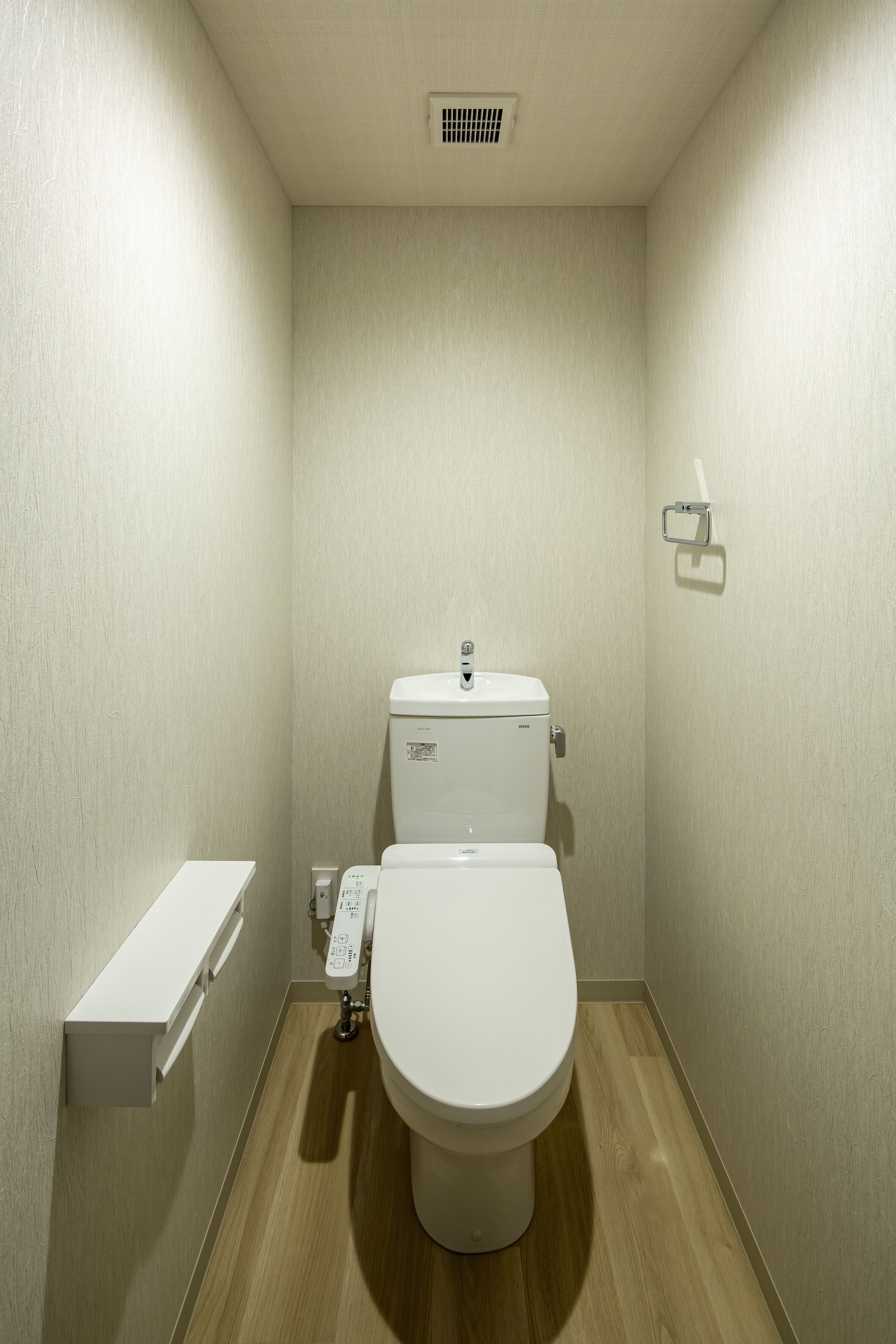 A small, modern bathroom with a toilet, a wall-mounted shelf, and a light switch.