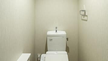 A small, modern bathroom with a toilet, a wall-mounted shelf, and a light switch.